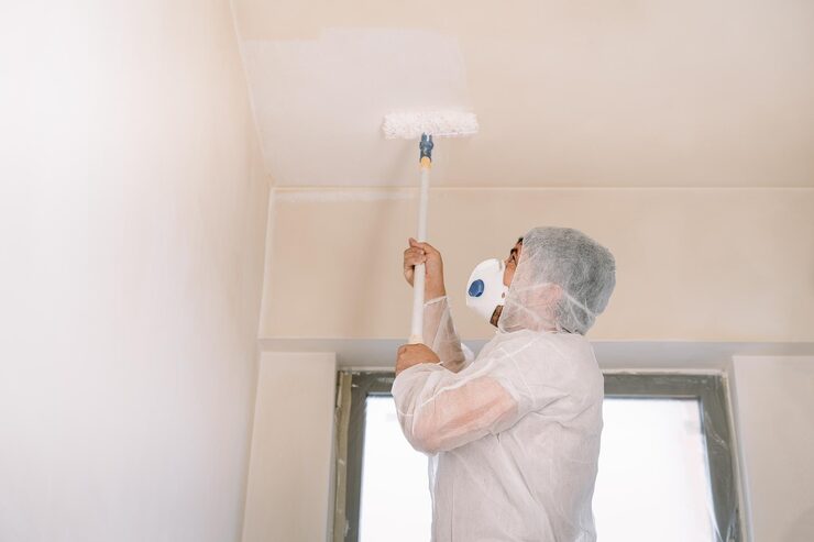 person with protective gear painting ceiling