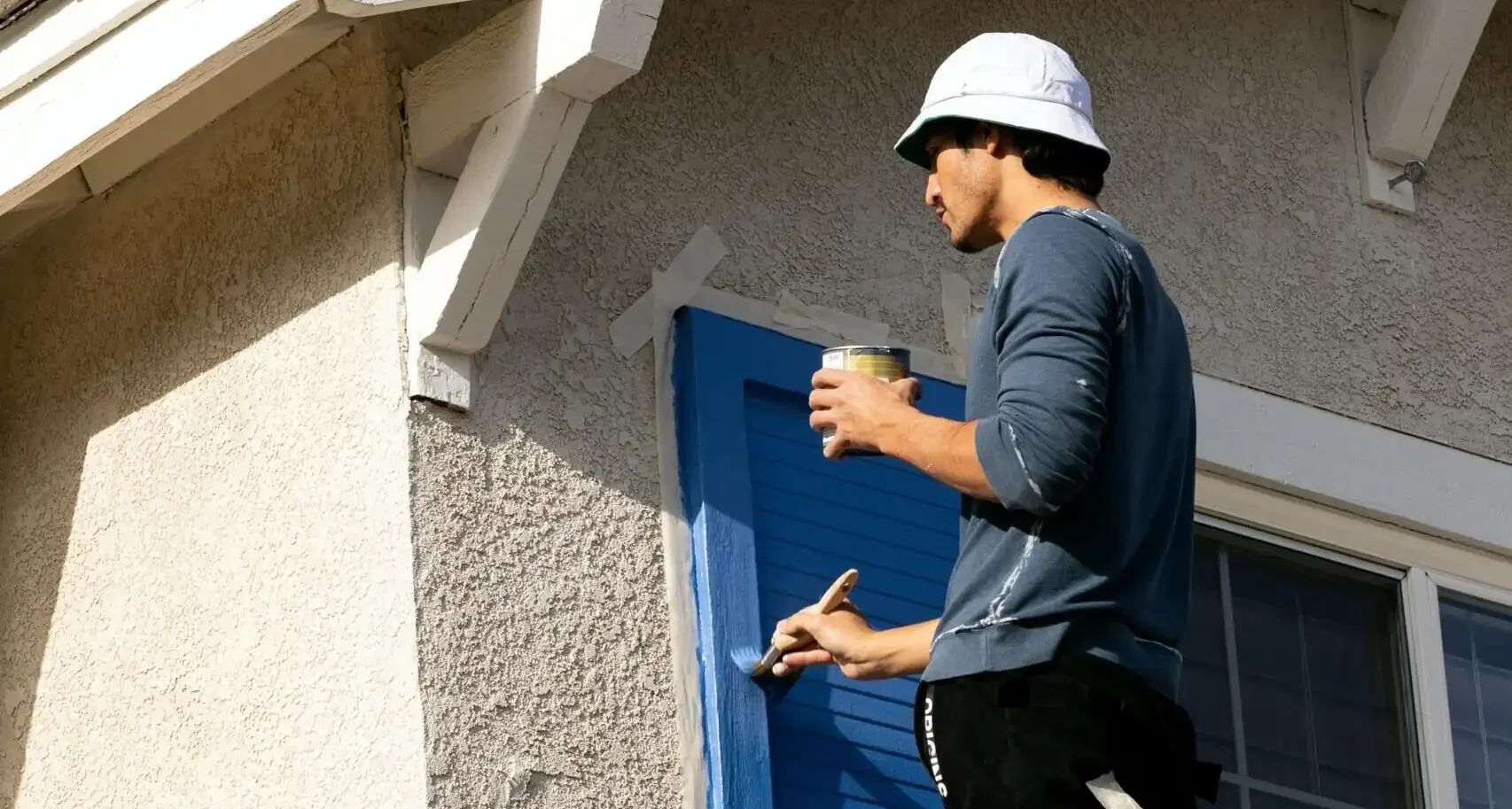 A professional painter meticulously painting exterior shutters a vibrant blue, helping homeowners calculate the total house painting cost in Fairfield, CT, for high-end curb appeal.