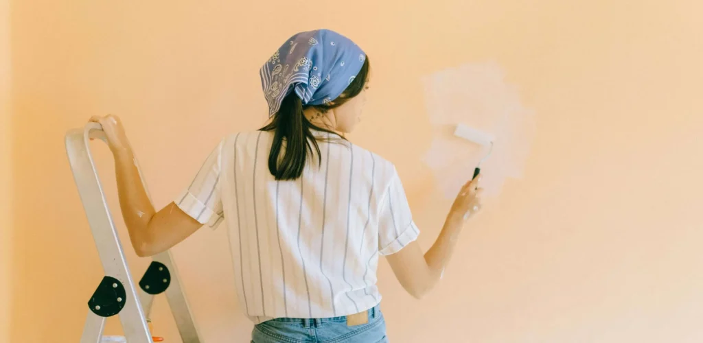 A professional painter on scaffolding applies a bold red finish to a brick exterior, showcasing the precision required during the best time of year to paint your home in Fairfield, CT for maximum curb appeal.