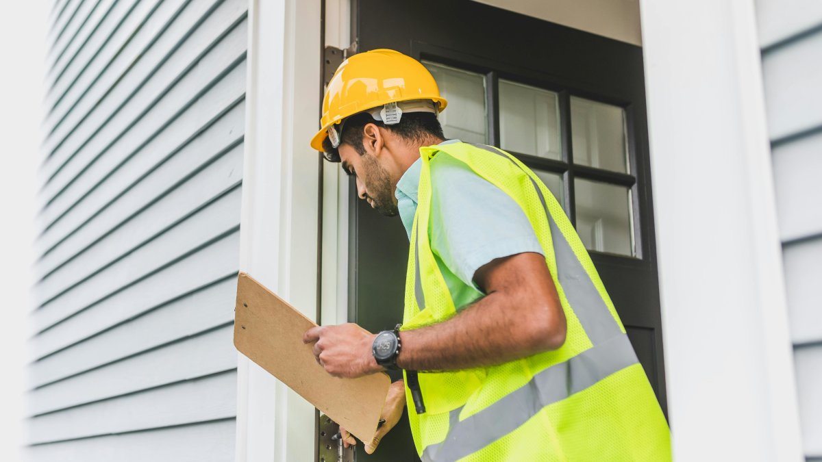 Inspector in hard hat performing outdoor property inspection with clipboard